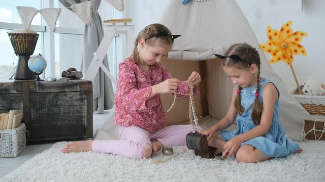 Little sisters playing with jewelry box sitting on floor in room