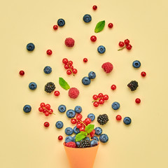 Blueberry, blackberry, raspberry, redcurrant in ice cream cone. Fresh blueberry, berries mix on yellow. Red raspberry, mint creative composition. Colorful minimal concept, top view.