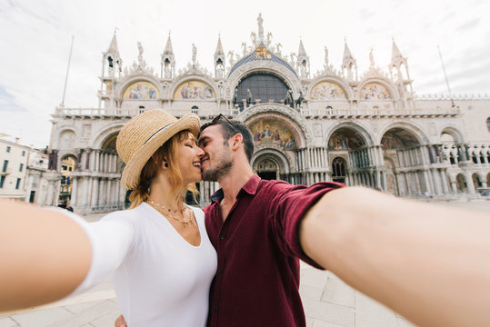 Young couple of lovers taking a selfie portrait at San Marco Square in Venice, Italy. Loving people are kissing outdoor.