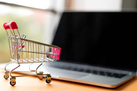 Close-Up Of Laptop And Shopping Cart By Credit Card On Table
