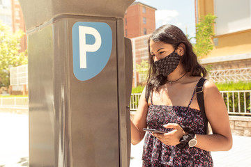 Young latin woman paying with the smartphone on the parking payment machine.