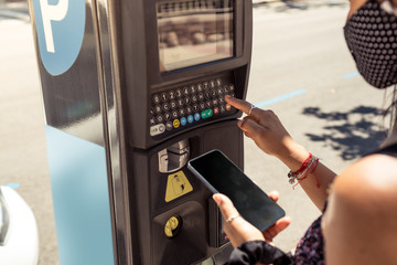Close up photography of woman using parking meter machine with the smartphone.