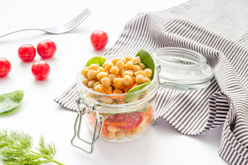 Vegan lunch. Chickpeas, carrot, tomato in glass jar on white table