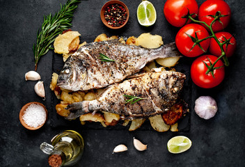 fried dorado fish and potatoes with ingredients on stone background