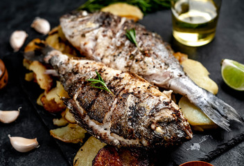 fried dorado fish and potatoes with ingredients on stone background