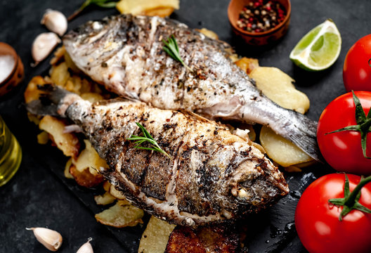 fried dorado fish and potatoes with ingredients on stone background