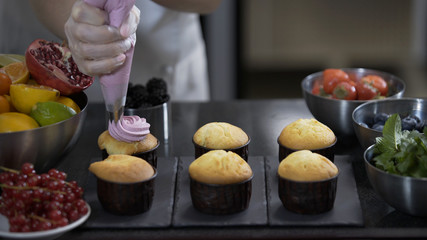 Decorating cup cake with cream. Using cooking bag, confectioner making muffins. Modern desserts and cakes. Cupcakes with cream filling. Professional pastry.