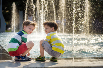 Cute toddler boy and older brothers, playing on a jet fountains with water splashing around,...