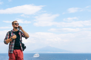 Male tourist takes the call. Shares impressions and information, uses a smartphone. Communication and mobile internet concept. 5g. View of the sea and Mount Vesuvius. Ocean liner. Copy space