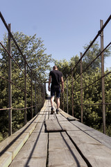 A young man walking on a wooden bridge, summer forest on the background. Selective focus.