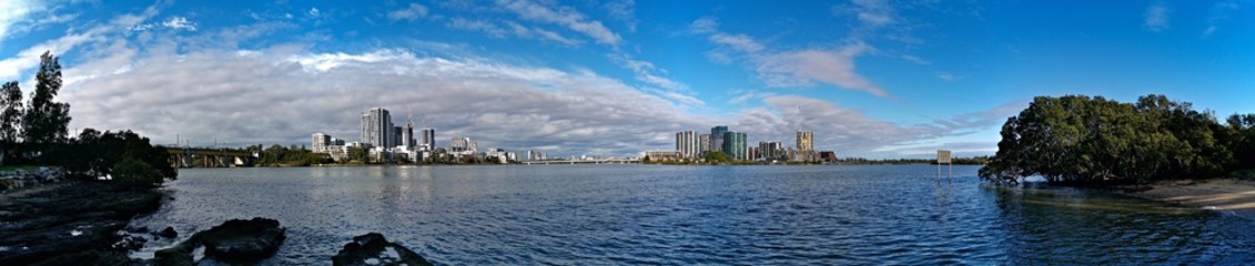 Fototapeta na wymiar Beautiful panoramic view of high-rise buildings on the riverbank on a sunny day with deep blue sky and light clouds, Parramatta river, Meadowbank, Sydney, New South Wales, Australia 