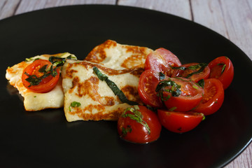 halloumi cheese with tomatoes and basil on a black plate
