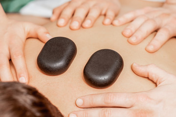 Close up massage therapists hands doing back massage with hot stones on back of man in spa.