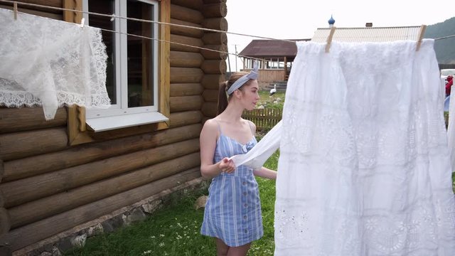 Girl in a blue dress with long hair washes clothes and linen on her hands outdoors
