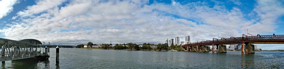 Fototapeta na wymiar Beautiful panoramic view of a wharf and a railway bridge across a river on a sunny day with deep blue sky, Parramatta river, Meadowbank, Sydney, New South Wales, Australia 
