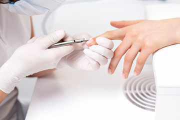 Close up of manicurist using manicure cutter to remove cuticle of female nails in manicure salon