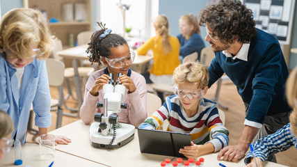 Elementary School Science Classroom: Cute Little Girl Looks Under Microscope, Boy Uses Digital...