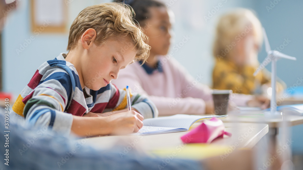 Poster in elementary school classroom brilliant caucasian boy writes in exercise notebook, taking test and 