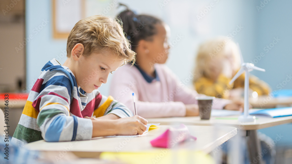 Poster in elementary school classroom brilliant caucasian boy writes in exercise notebook, taking test and 