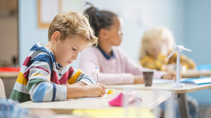 In Elementary School Classroom Brilliant Caucasian Boy Writes in Exercise Notebook, Taking Test and...