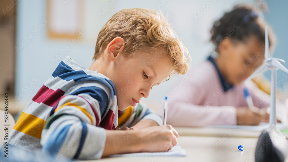 Poster in elementary school classroom brilliant caucasian boy writes in exercise notebook, taking test and 