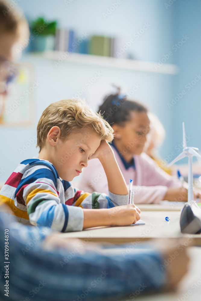 Poster in elementary school classroom brilliant caucasian boy writes in exercise notebook, taking test and 