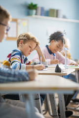 In Elementary School Classroom Brilliant Caucasian Boy Writes in Exercise Notebook, Taking Test and...