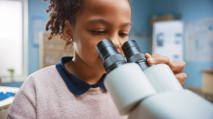 Portrait of Smart Little Schoolgirl Looking Under the Microscope. In Elementary School Classroom Cute Girl Uses Microscope. STEM (science, technology, engineering and mathematics) Education Program