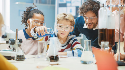 Elementary School Science Classroom: Little Boy Mixes Chemicals in Beakers. Enthusiastic Teacher Explains Chemistry to Diverse Group of Children. Children Learn with Interest