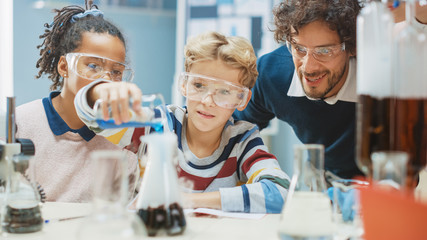 Elementary School Science Classroom: Little Boy Mixes Chemicals in Beakers. Enthusiastic Teacher Explains Chemistry to Diverse Group of Children. Children Learn with Interest