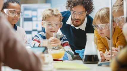 Elementary School Science Classroom: Enthusiastic Teacher Explains Chemistry to Diverse Group of Children, Little Boy Mixes Chemicals in Beakers. Children Acqaering Knowledge