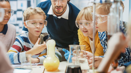 Elementary School Science Classroom: Enthusiastic Teacher Explains Chemistry to Diverse Group of Children, Little Boy Mixes Chemicals in Beakers. Children Acqaering Knowledge