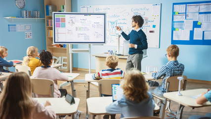 Fototapeta Elementary School Science Teacher Uses Interactive Digital Whiteboard to Show Classroom Full of Children how Software Programming works for Robotics. Science Class, Curious Kids Listening Attentively obraz