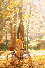 Stylish woman with a bicycle enjoying autumn weather in the park. Beautiful Woman walking  in the autumn forest.