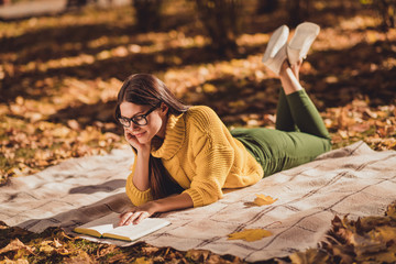 Full size profile side photo of focused positive girl rest relax countryside autumn forest lying checkered blanket read book wear yellow color jumper