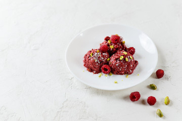 Raspberry ice cream from aquafaba with pistachios on a white plate. Horizontal orientation, copy space. Sugar, lactose, gluten free.