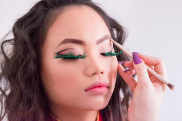 Make-up Artist Contouring the Eyebrows, on Asian Young Woman's Face with Make-up Brush, on White Background