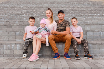 Fototapeta premium A stylish family of five sit on the steps and look into the camera. happy parents and three children