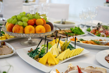 Beautiful table setting in light colors with dishes and assorted food on a table with a white tablecloth for a party, wedding or other special event. Restaurant business and service industry concept.