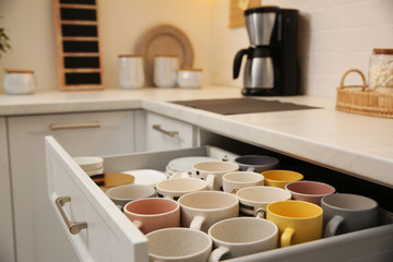 Fototapeta na wymiar Open drawer with cups and coffeemaker on countertop in kitchen