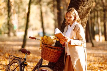 Stylish woman reading a book in the autumn park. Relaxation, enjoying, solitude with nature.