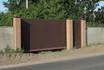 brown iron closed gate and part of a gray concrete fence on the street by an asphalt road