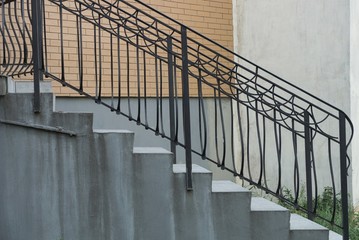 Staircase with gray concrete steps and iron black handrails with a forged pattern near the wall