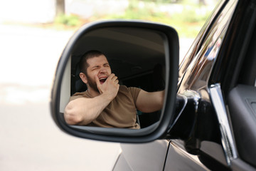 Tired man yawning in his auto, view through car side mirror