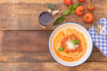 Top view of spagetties bolonaise sauce with yellow pasta, garlic, basil leaves, and tomatoes on wooden table background with copy space for text.