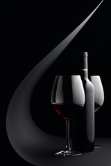 Bottle and glasses of red wine on a black background.