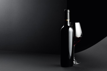 Bottle and glass of red wine on a dark background.