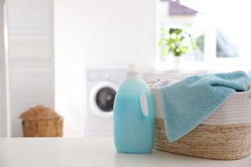 Wicker basket with towels and detergent on white table indoors. Space for text