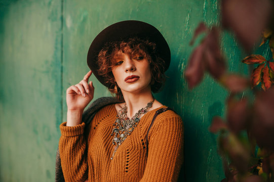 Autumn fashion portrait of a model with curly short hair on a green grunge background, wears vintage clothes and looks away with a serious face. Fashionable rural girl posing.