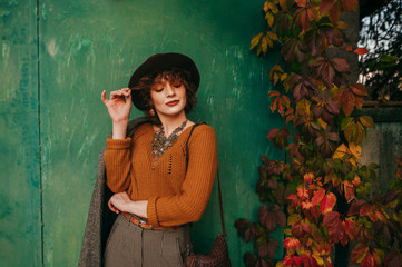 Fashion portrait of attractive lady in vintage clothes against green grunge autumn wall background,looking down and to the side and smiling. Photo of attractive girl from village on grunge background.